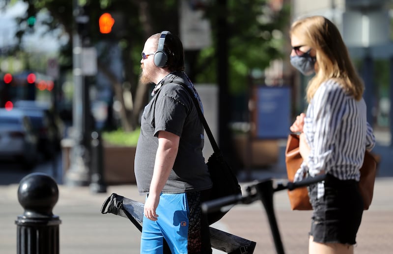 A maskless pedestrian and a pedestrian wearing a mask walk in Salt Lake City on Friday, May 14, 2021.
