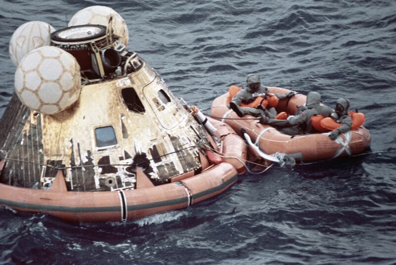 U.S. Navy personnel, protected by Biological Isolation Garments, are recovering the Apollo 11 crew from the re-entry vehicle, which landed safely in the Pacific Ocean on July 24, 1969, after an eight-day mission on the moon.