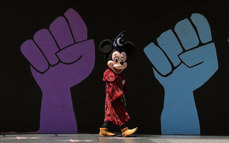 A person dressed as Mickey Mouse walks by a mural in Los Angeles.