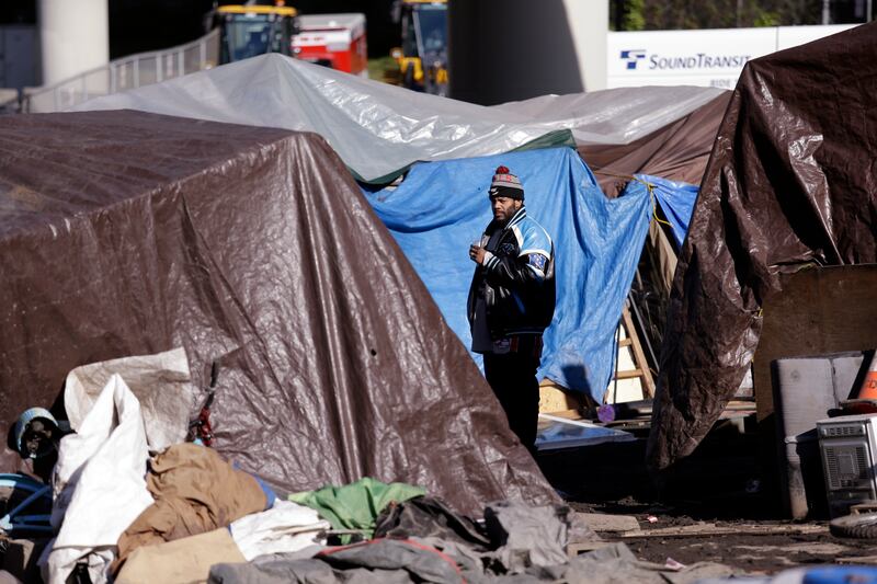 In this photo taken March 6, 2017, a man looks out between tarp-covered tents in a homeless encampment that the city was to remove the following day, in Seattle. Sixteen months after he declared a state of emergency on homelessness, Seattles mayor is aski