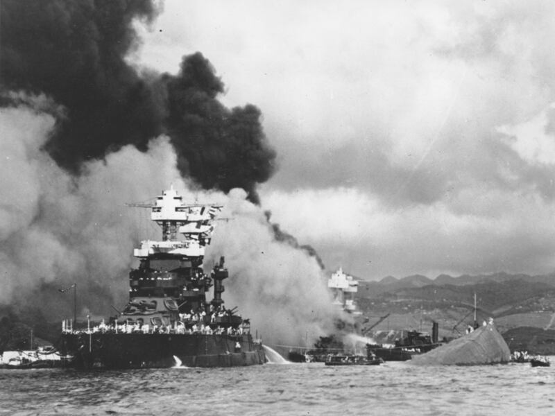 In this Dec. 7, 1941, file photo, part of the hull of the capsized USS Oklahoma is seen at right as the battleship USS West Virginia, center, begins to sink after suffering heavy damage during the attack on Pearl Harbor.