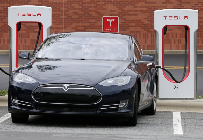 FILE- In this June 24, 2017, file photo, a Telsa Model 3 car recharges at a Tesla charging station at Cochran Commons shopping center in Charlotte, N.C.