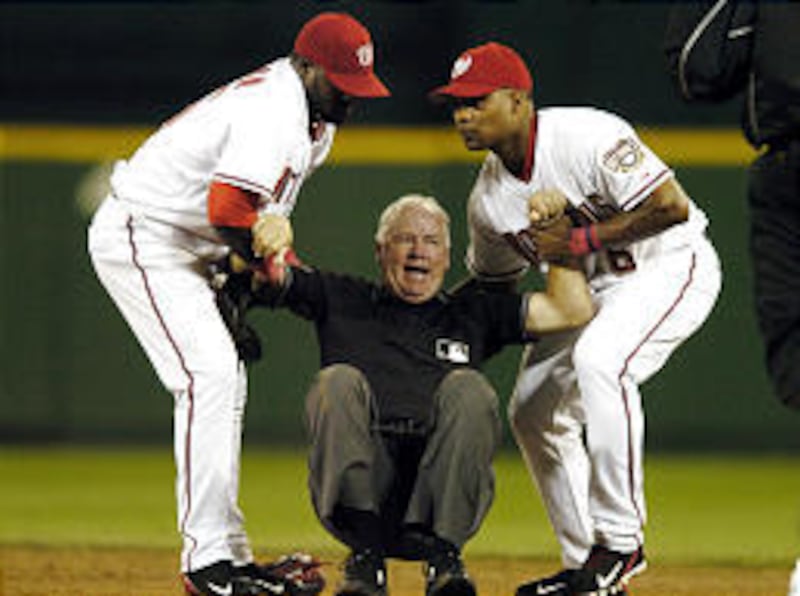 Washington's Cristian Guzman, left, and Jose Guillen help up second base umpire Joe Brinkman.