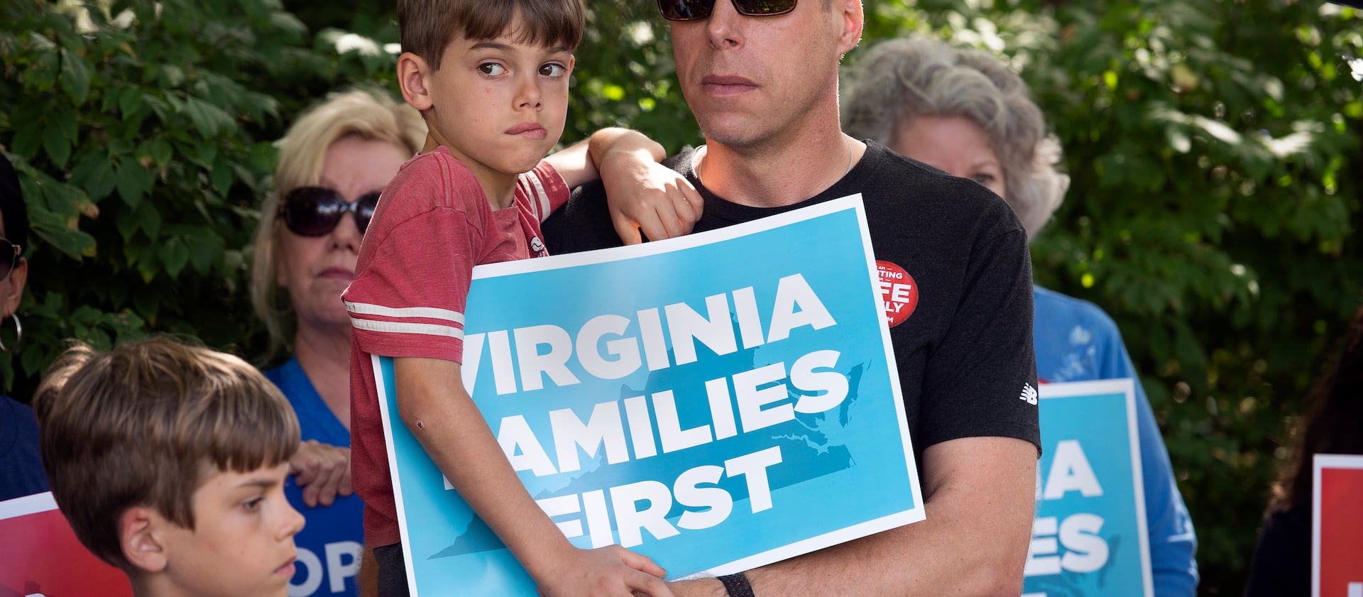 Patrick Novecosky holds son Daniel as son Peter stands beside them during a rally tied to the Virginia governor’s race.