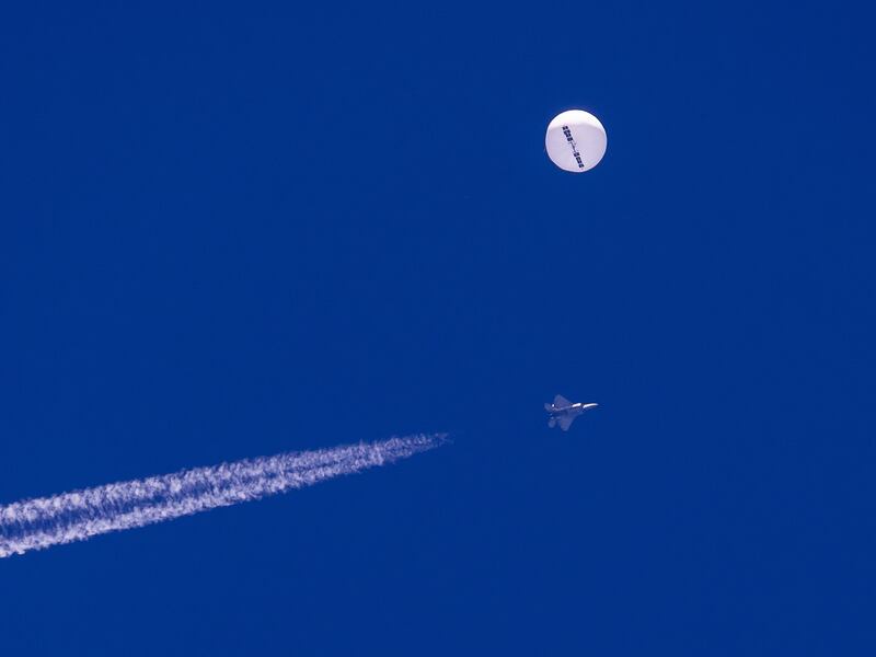A large balloon drifts above the Atlantic Ocean, just off the coast of South Carolina, with a fighter jet and its contrail seen below it.