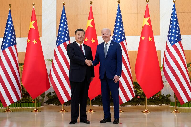 Chinese President Xi Jinping shakes hands with U.S. President Joe Biden in front of a row of Chinese flags and American flags.