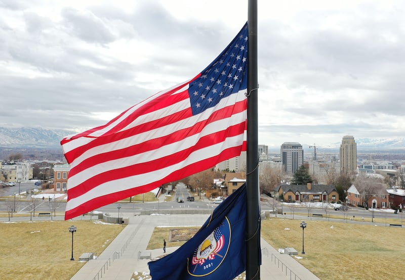 An American flag and a Utah state flag fly with Salt Lake City in the background on an overcast day.