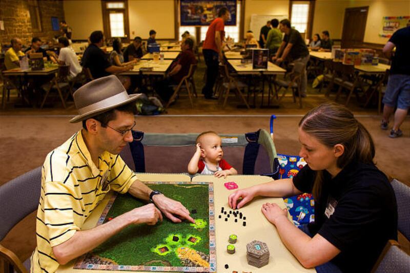 Scott Neves, with son Thomas, teaches Jennifer Loveland how to play Tikal at the University of Utah officers club Saturday.