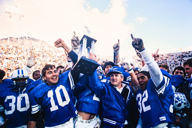BYU coach LaVell Edwards holding conference championship trophy with punter Lee Johnson (No. 10) on Nov. 24, 1984.