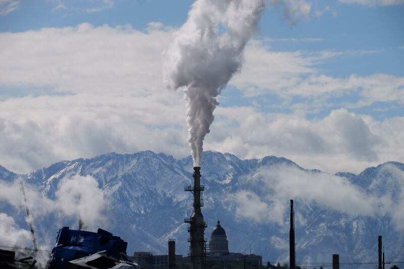 plumes fill the sky from an oil refinery with the Utah State Capitol in the background.