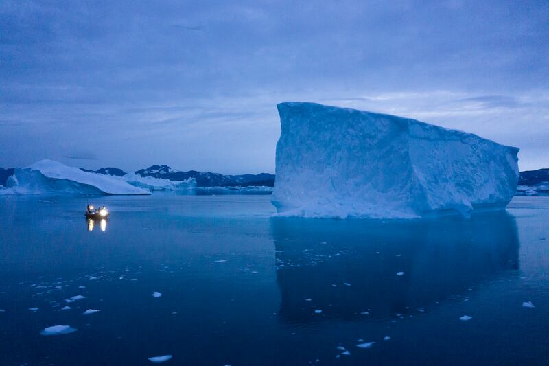 A boat navigates at night next to large icebergs in eastern Greenland on Aug. 15, 2019.