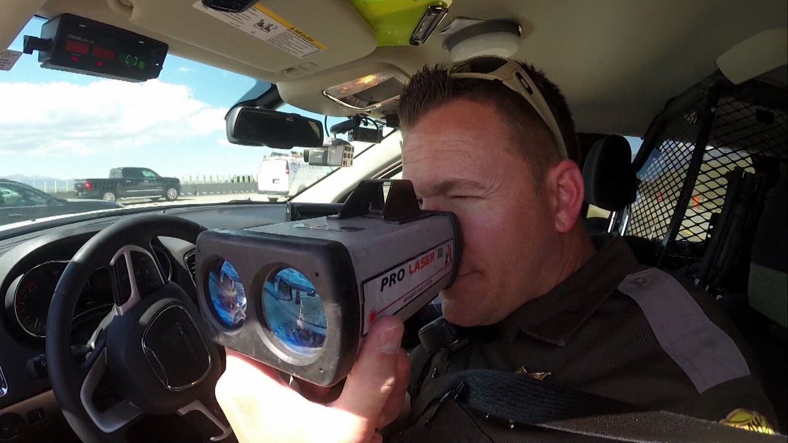 A Utah Highway Patrol trooper uses a radar gun to watch for speeding drivers.