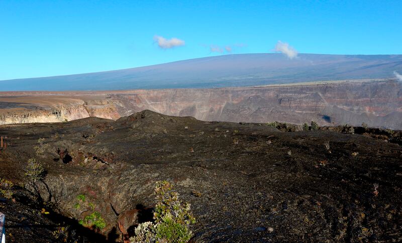 In this April 25, 2019 photo, Hawaii's Mauna Loa volcano, background, towers over the summit crater of Kilauea volcano in Hawaii Volcanoes National Park on the Big Island. Federal officials raised the alert level for Mauna Loa, the world's largest active
