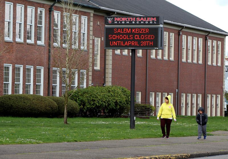 A woman and child walk past a North Salem High School in Salem, Ore., March 31, 2020, which like all schools in Oregon is closed because of the coronavirus.