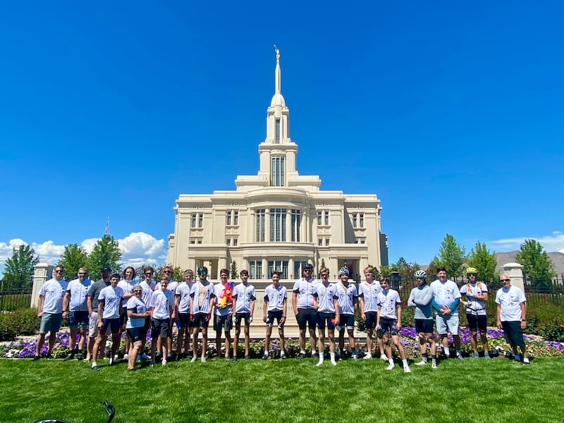 A group of Latter-day Saint young men and adults stand in front of the Payson Utah Temple on a clear day with blue skies.