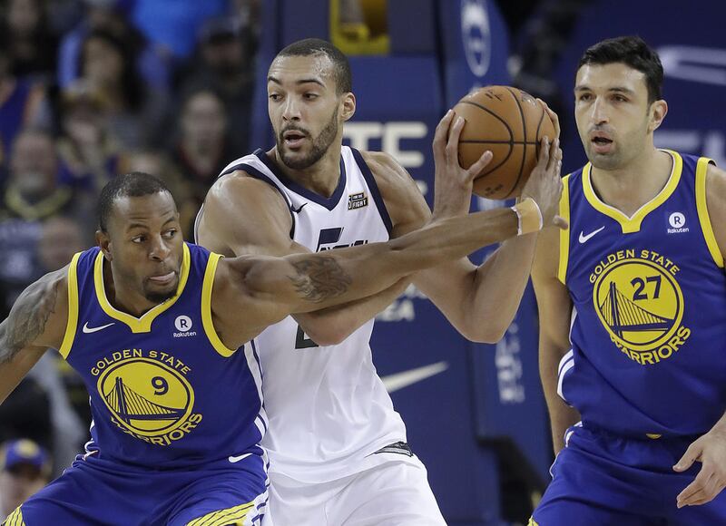 Utah Jazz center Rudy Gobert, center, looks to pass between Golden State Warriors forward Andre Iguodala (9) and center Zaza Pachulia (27) during the first half of an NBA basketball game in Oakland, Calif., Sunday, March 25, 2018. (AP Photo/Jeff Chiu)