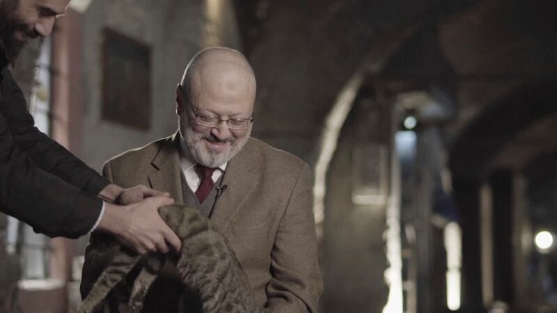In this image made from a March 2018 video provided by Metafora Production, Eiad Alhaji, a Syrian documentary film maker, grabs a cat that jumped onto Jamal Khashoggi's lap as he speaks in an interview at an undisclosed location. Eighteen days after Khash