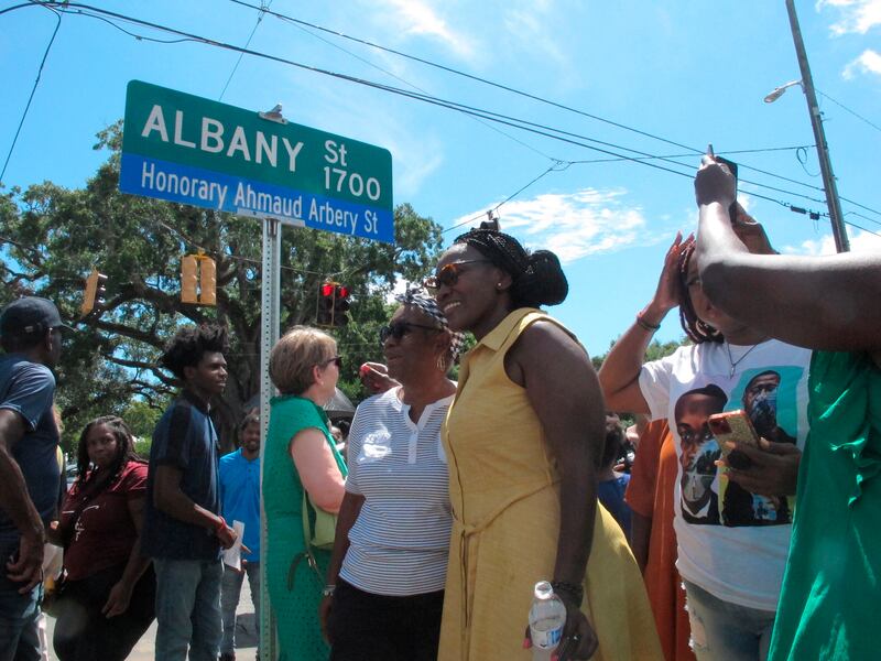 Wanda Cooper-Jones (on right in yellow dress) poses for photos with supporters beneath a new street sign honoring her son, Ahmaud Arbery.