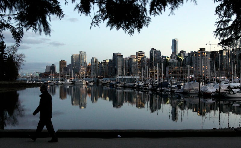 A man walks in Stanley Park as the skyline of Vancouver is reflected in water.