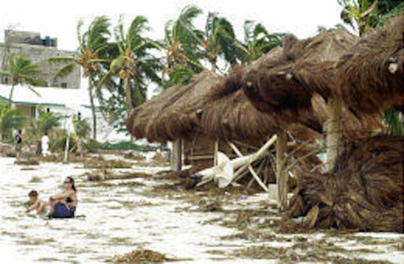 Tourists sit amid destroyed huts on the beach in Playa del Carmen, about 40 miles south of Cancun, after Hurricane Emily passed over Mexico's Cancun Peninsula Monday. The hurricane hit the peninsula with 145 mph winds, causing widespread damage. No deaths