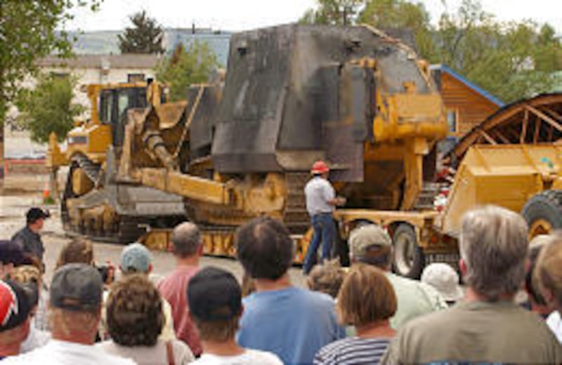 Onlookers watch as the armored bulldozer is loaded onto a tractor-trailer after being pulled from the rubble of a warehouse. At least six buildings were destroyed.