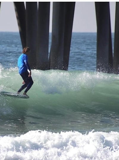 Saxon Baltzer hangs 10 while riding a wave near a pier in California.