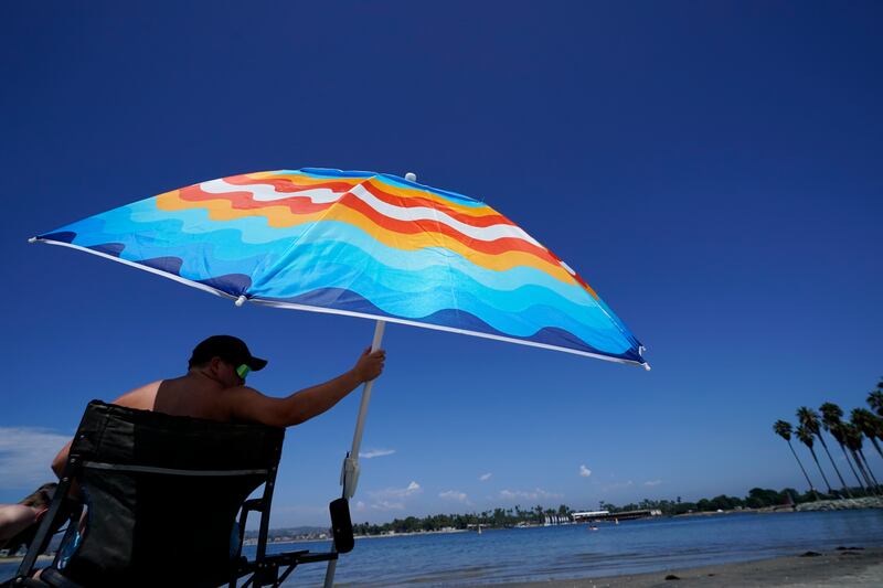 Seth Salmond, of Alpine, California, cools off under an umbrella along Mission Bay on Friday, Sept. 2, 2022, in San Diego.
