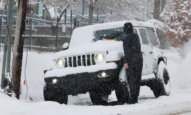 A driver brushes snow off their windshield as snow falls in Salt Lake City on Tuesday, Dec. 13, 2022.