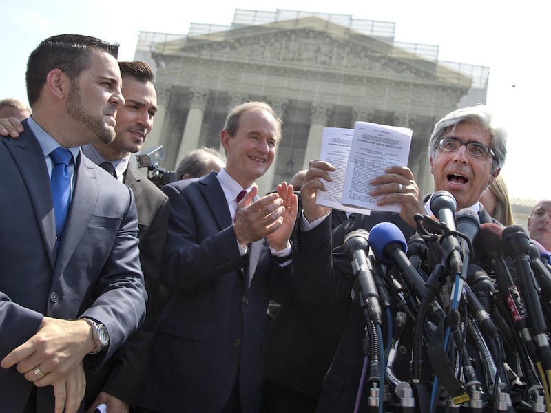 Attorney Ted Boutrous, right, holds copies of the Supreme Court decisions in Hollingsworth v. Perry, and United States v. Windsor, with plaintiffs Jeff Zarrillo, far left, and his partner Paul Katami, second from left, at a news conference on the court's