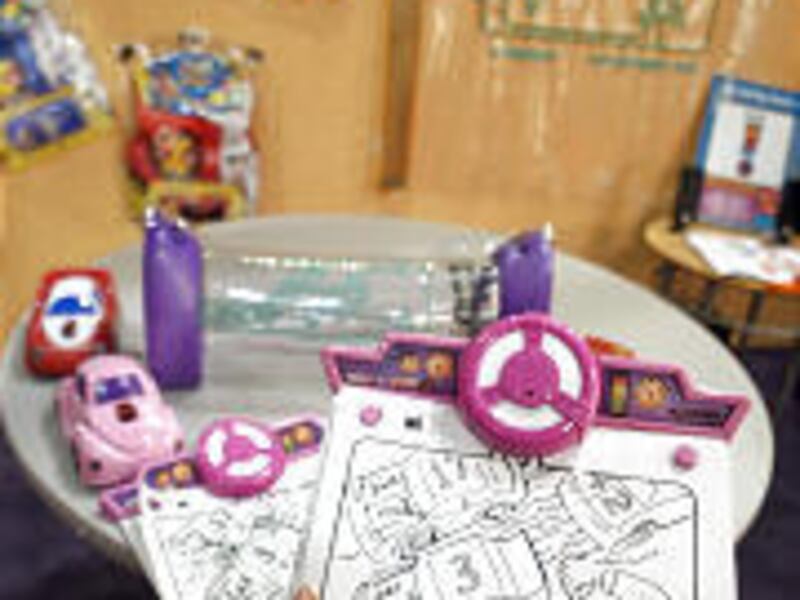 T-ink items include a touch sensitive Color 'N Drive, foreground; an Airwavez radio, Fast Lane Tinker-active cars and vests, on the table; and a large version of a printed circuit board on the wall, background.