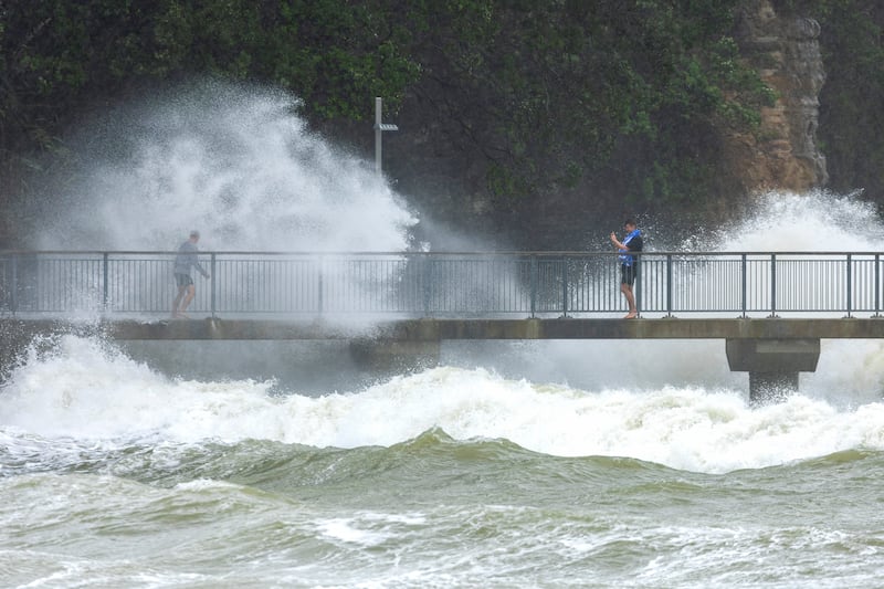 People watch as waves crash against the cliffs at an Auckland beach as a cyclone hits the upper parts of New Zealand.