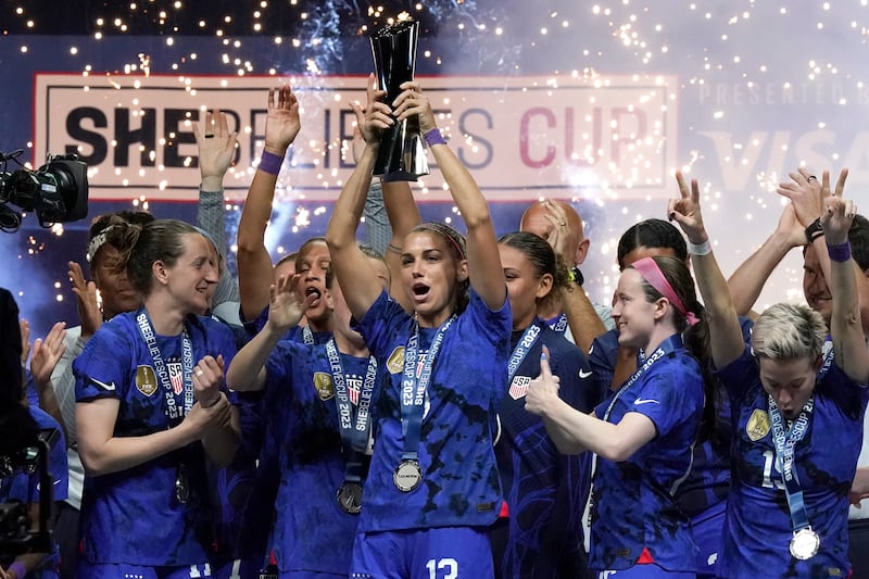 U.S. forward Alex Morgan, center, lifts the SheBelieves Cup with teammates after they won a soccer match against Brazil.