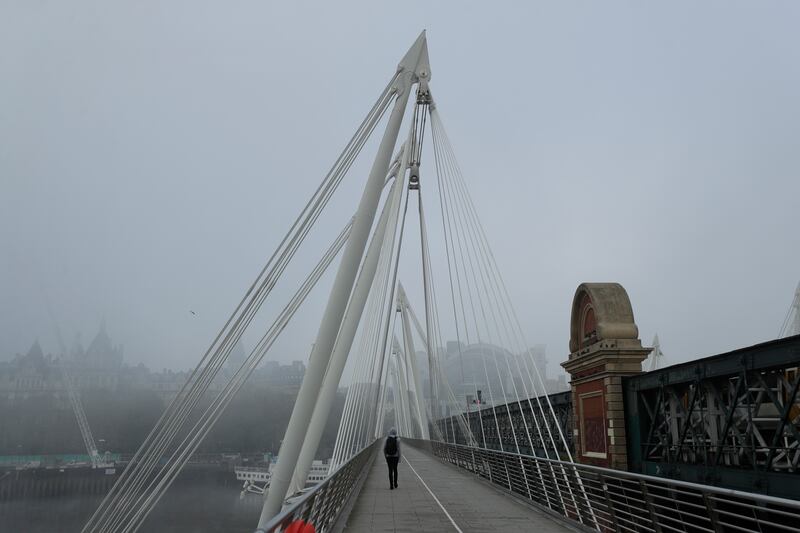 In this Thursday, Nov. 5, 2020 file photo, a person walks in fog over one of the pedestrian Golden Jubilee Bridges, on the first day of Britain’s second lockdown designed to save its health care system from being overwhelmed by people with coronavirus, in London.
