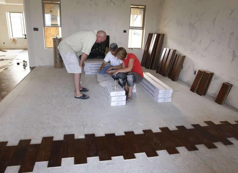 Kevin and Steffani Raff take a moment to sign mortgage papers with their broker, Rick Lyman, as they are laying their own wood floor to help them save money while building their new home this past summer in Saratoga Springs, Utah. Forty percent of those o