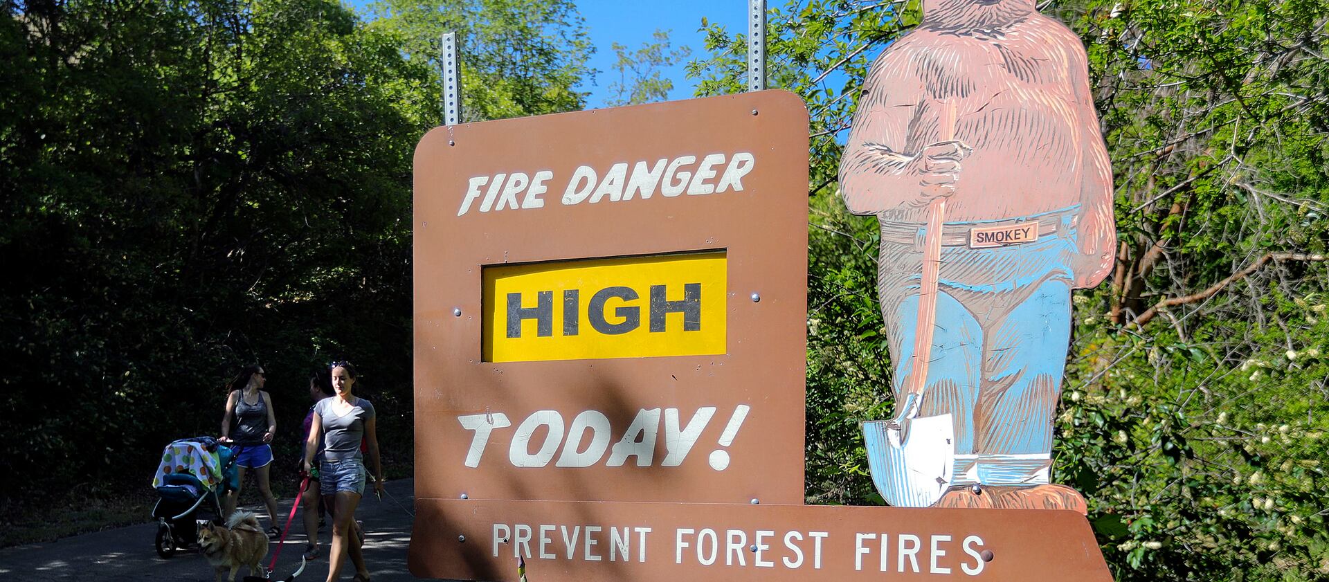 A fire danger sign is shown reading “High” in City Creek Canyon in Salt Lake City as two people walk by.