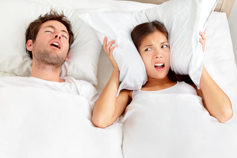 A man and woman in bed while the woman covers her ears with a pillow.