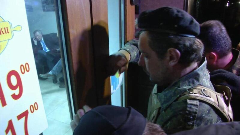 This image taken from AP video shows a group of unidentified men in military fatigues outside a cafe in Simferopol, Ukraine who appear to be stopping UN Special Envoy to Ukraine, Robert Serry from leaving as he makes a call on his mobile phone inside, Wed