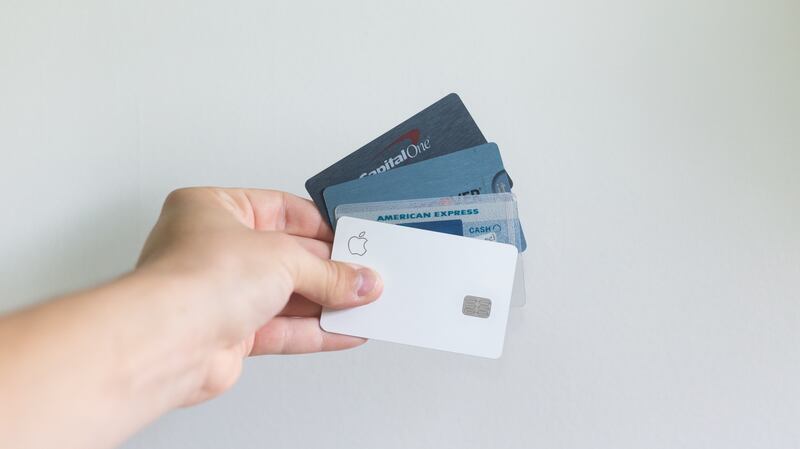 A hand holds an array of credit cards against a white background.