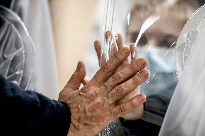 In this Dec. 22, 2020, file photo, relatives touch each other’s hand through a plastic film screen and a glass to avoid contracting COVID-19 at the San Raffaele center in Rome ahead of Christmas.