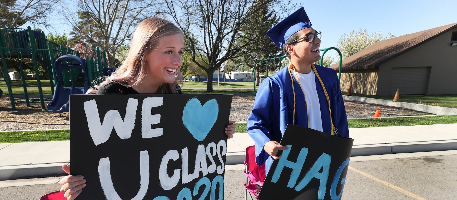 Students hold up signs sending well-wishes to the class of 2020 as graduating seniors pick up their caps, gowns, honor codes and yard signs in Pleasant Grove Utah in April 2020.