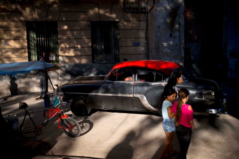 Girls walk along a street in Old Havana where a driver steers his classic American car in Havana, Cuba, Tuesday, April 17, 2018. A legislative session on Wednesday will see a historic political transition, in which President Raul Castro plans to step down