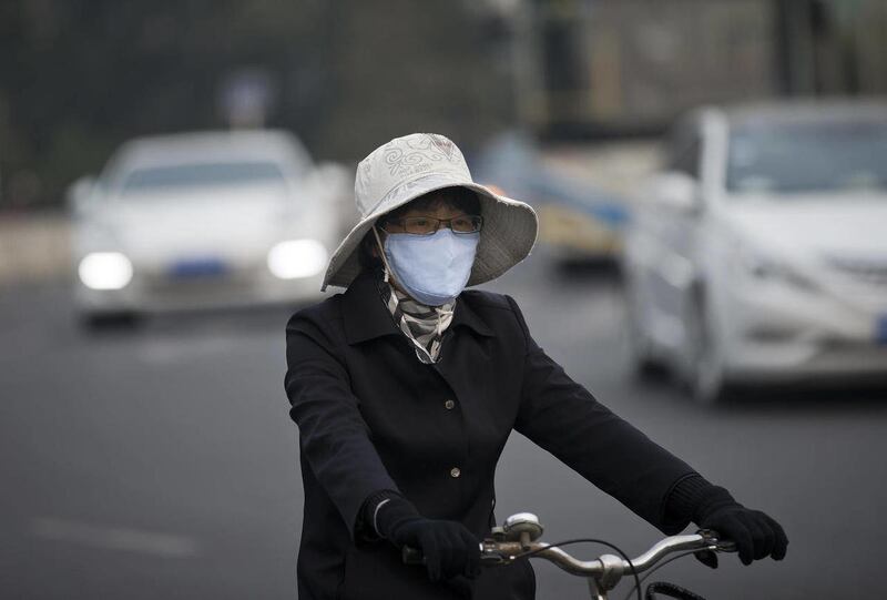 A woman wearing a face mask bicycles on a road in Beijing Tuesday, Oct. 22, 2013.