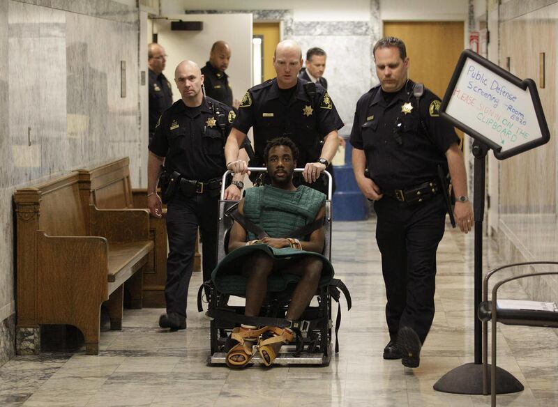 In this May 12, 2011 photo, accused rapist and murderer Isaiah Kalebu, lower center, is taken in a wheeled restraint chair through a hallway at the King County Courthouse following a court hearing in Seattle. Judge Michael C. Hayden has taken the unusual