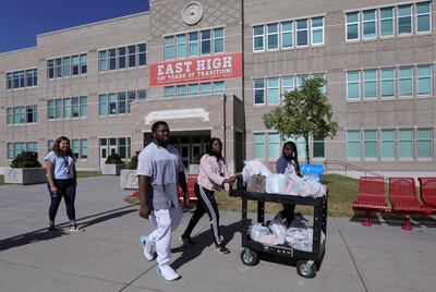 Karina Soto, family services assistant, helps Islam Djobo, Wali Djobo and Amida Djobo take a cartload of food from the Smith's East High Leopard Stash at East High School to their vehicle in Salt Lake City on Tuesday, June 18, 2019.