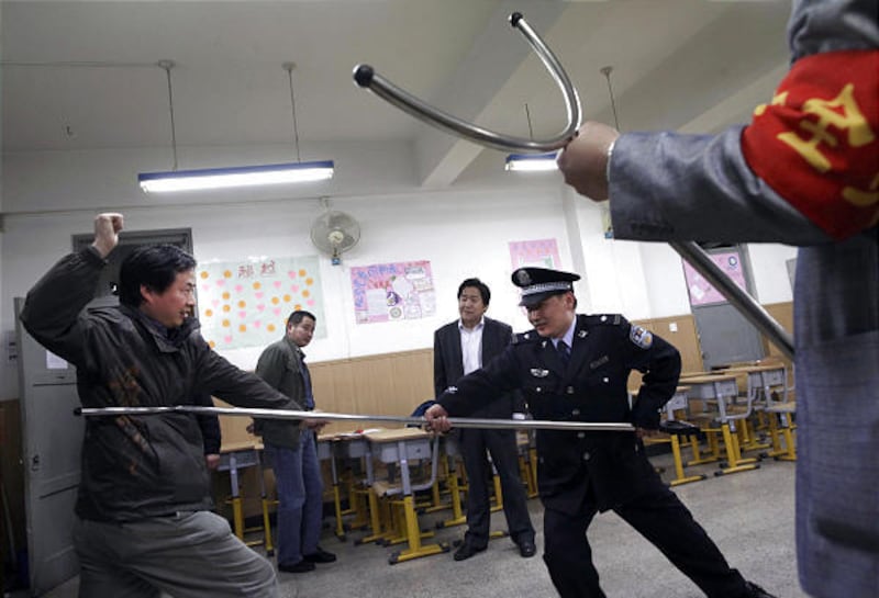 A Chinese police officer demonstrate the use of a "police restraint stick" long-handled poles with a hook on the end to subdue a man playing the role of an attacker at a middle school in Beijing Thursday.