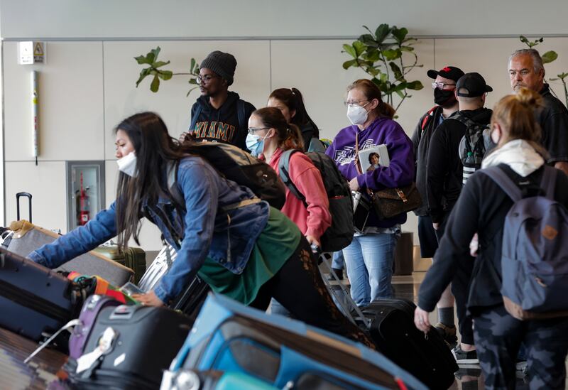 Masked and unmasked travelers wait for their luggage at the Salt Lake City International Airport.