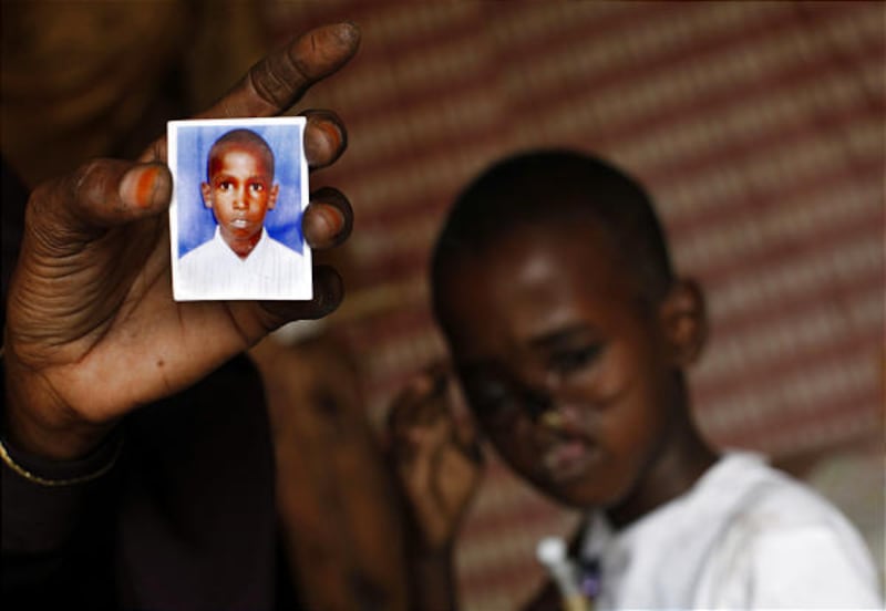 Ahmed Mohamed Mohamoud sits in a hotel in Nairobi, Kenya, as his mother, Safi Mohamed Shidane holds a photo of how the 8-year-old looked before he was hit by a bullet.