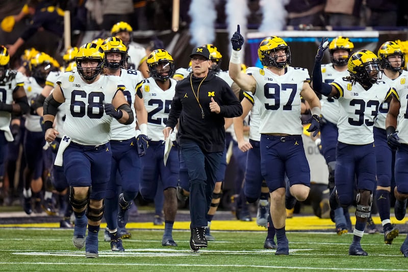 Michigan head coach Jim Harbaugh runs onto the field with his team before the Big Ten championship game in Indianapolis.