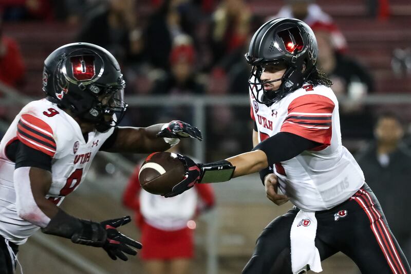Utah Utes quarterback Cameron Rising hands the ball off to running back Tavion Thomas.