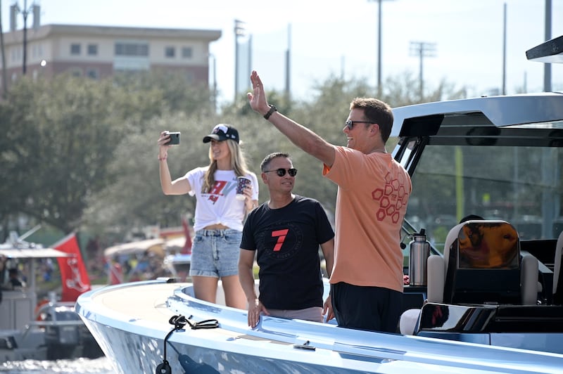 Tampa Bay Buccaneers quarterback Tom Brady waves to fans as his personal trainer Alex Guerrero, left, watches during a parade on Feb. 10, 2021, in Tampa, Fla.